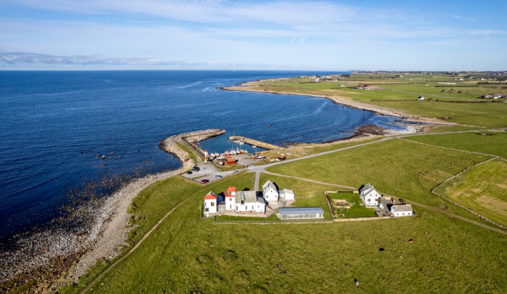 Dronebilde over fyr på Jæren. Kvassheim fyr, båthavn og jordbruksmarker en høstdag.