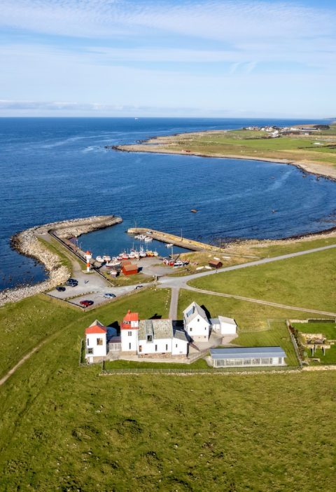 Dronebilde over fyr på Jæren. Kvassheim fyr, båthavn og jordbruksmarker en høstdag.