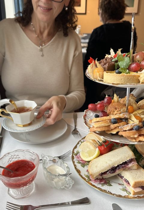 Afternoon tea på Jæren, kvinne heller te I en tekopp på et bord med kaker i et etasjefat.